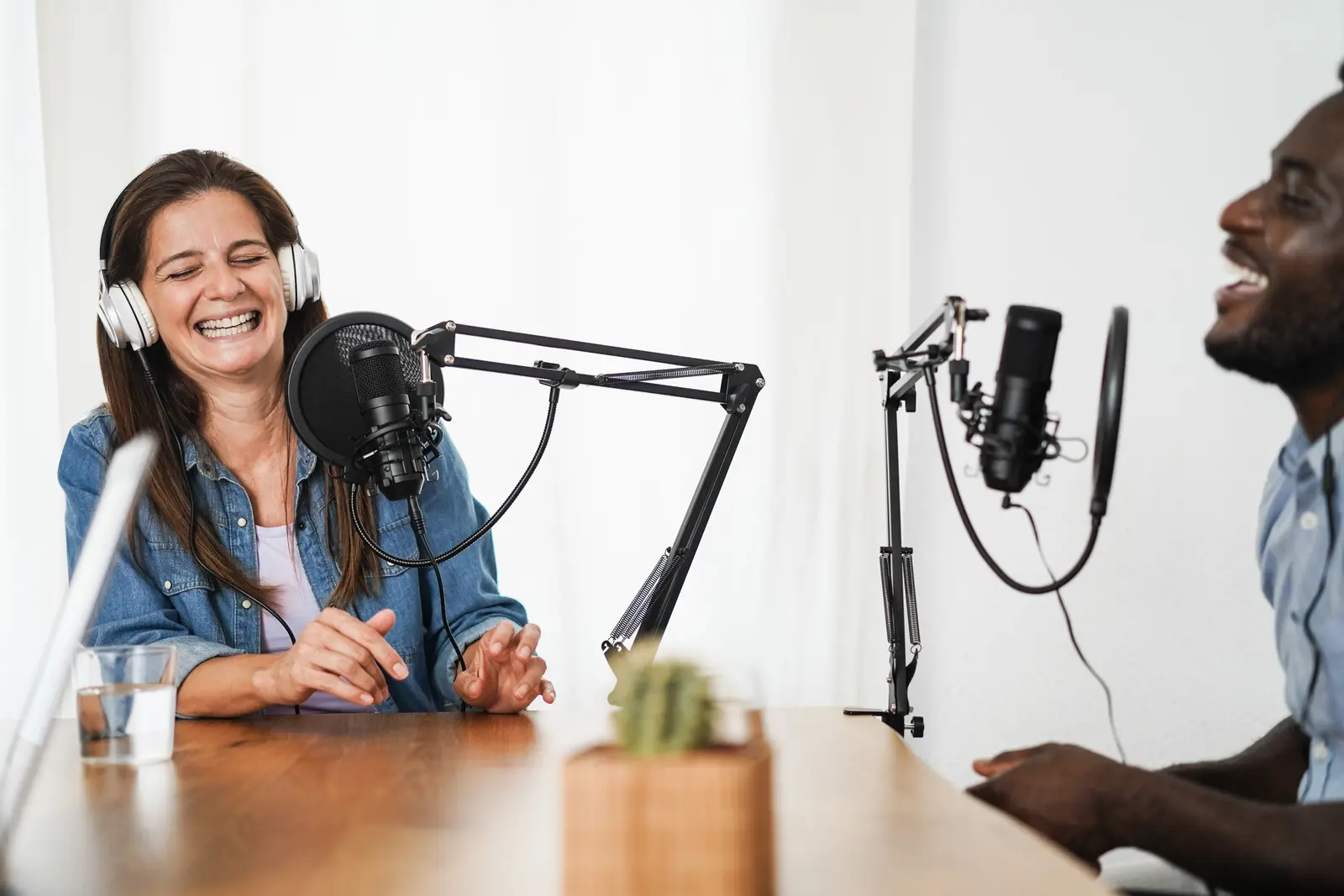 Two podcasters at studio microphones laughing during a recording session